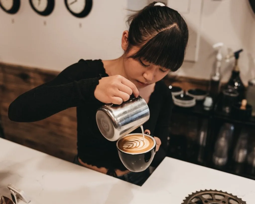 Barista gießt Milchschaum in eine Tasse und zieht ein Latte-Art-Muster