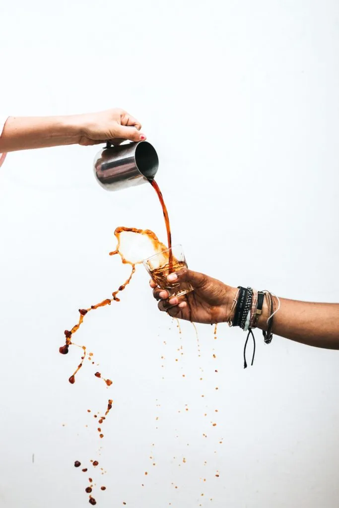 Kaffee wird aus einer Metallkanne in ein Glas gegossen und spritzt über den Rand