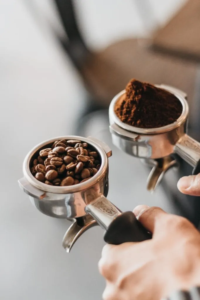 Zwei Siebträger in der Hand: einer mit ganzen Kaffeebohnen, einer mit frisch gemahlenem Espressomehl
