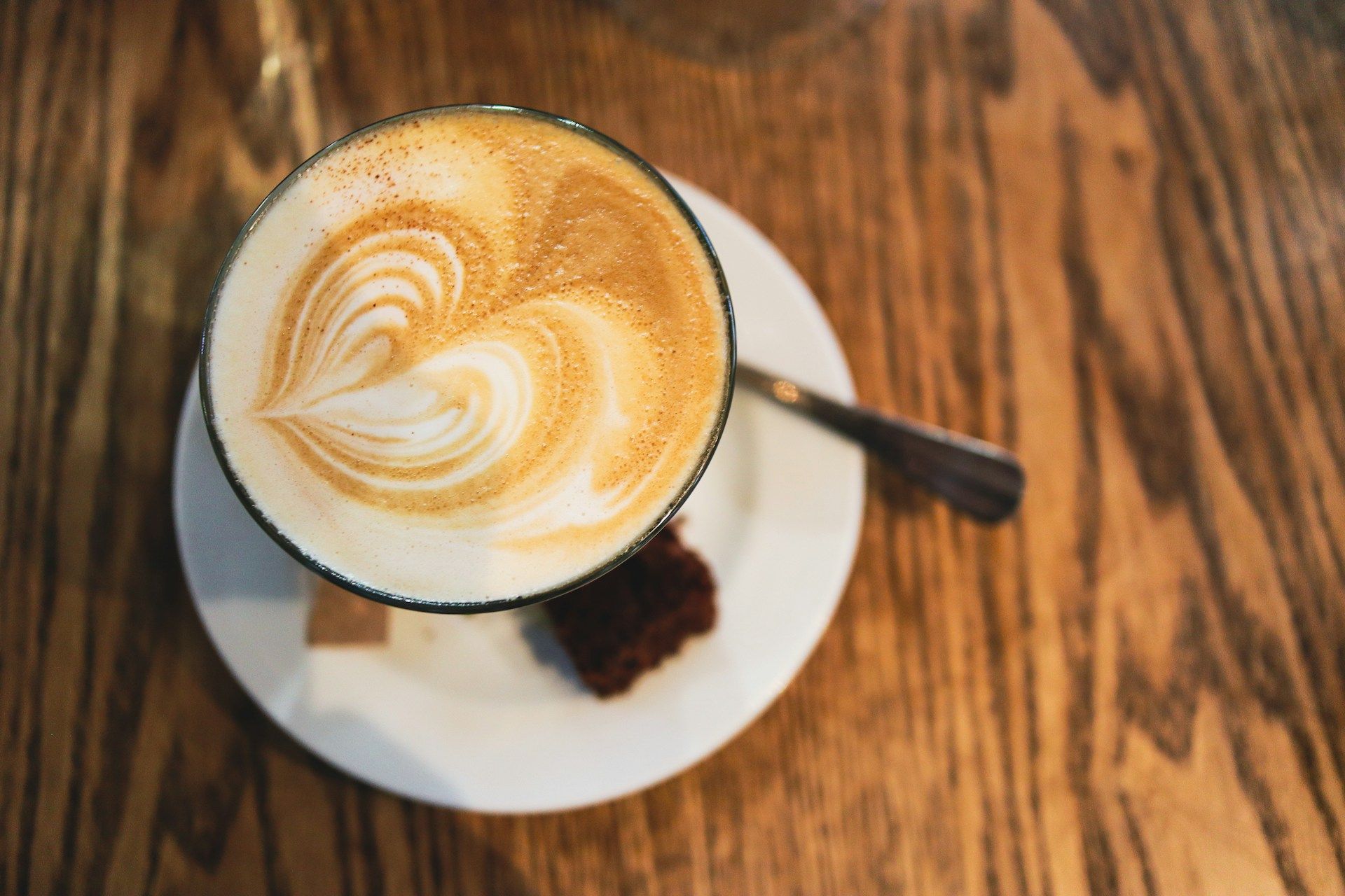 Cappuccino mit Latte Art und ein Stück Brownie auf einem Holztisch