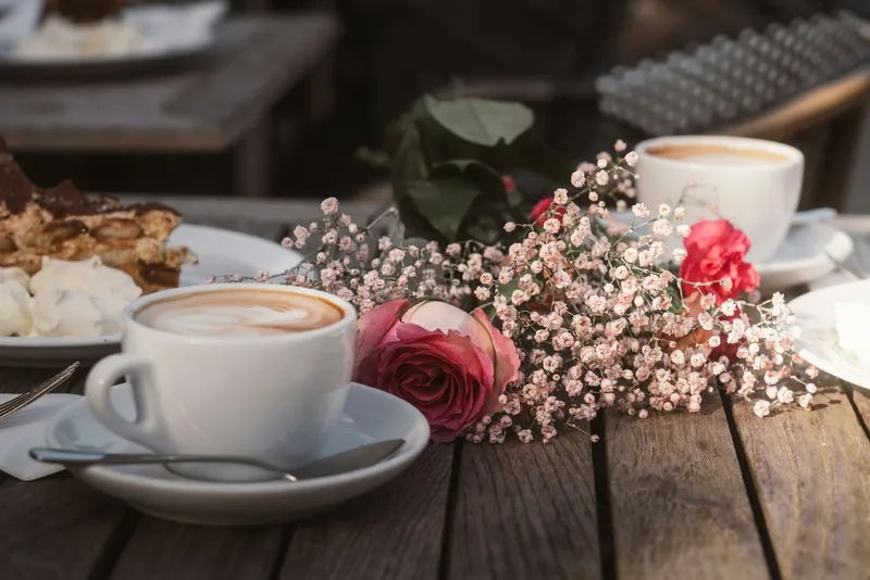 Cappuccino neben einer Rose und Schleierkraut auf einem Holztisch