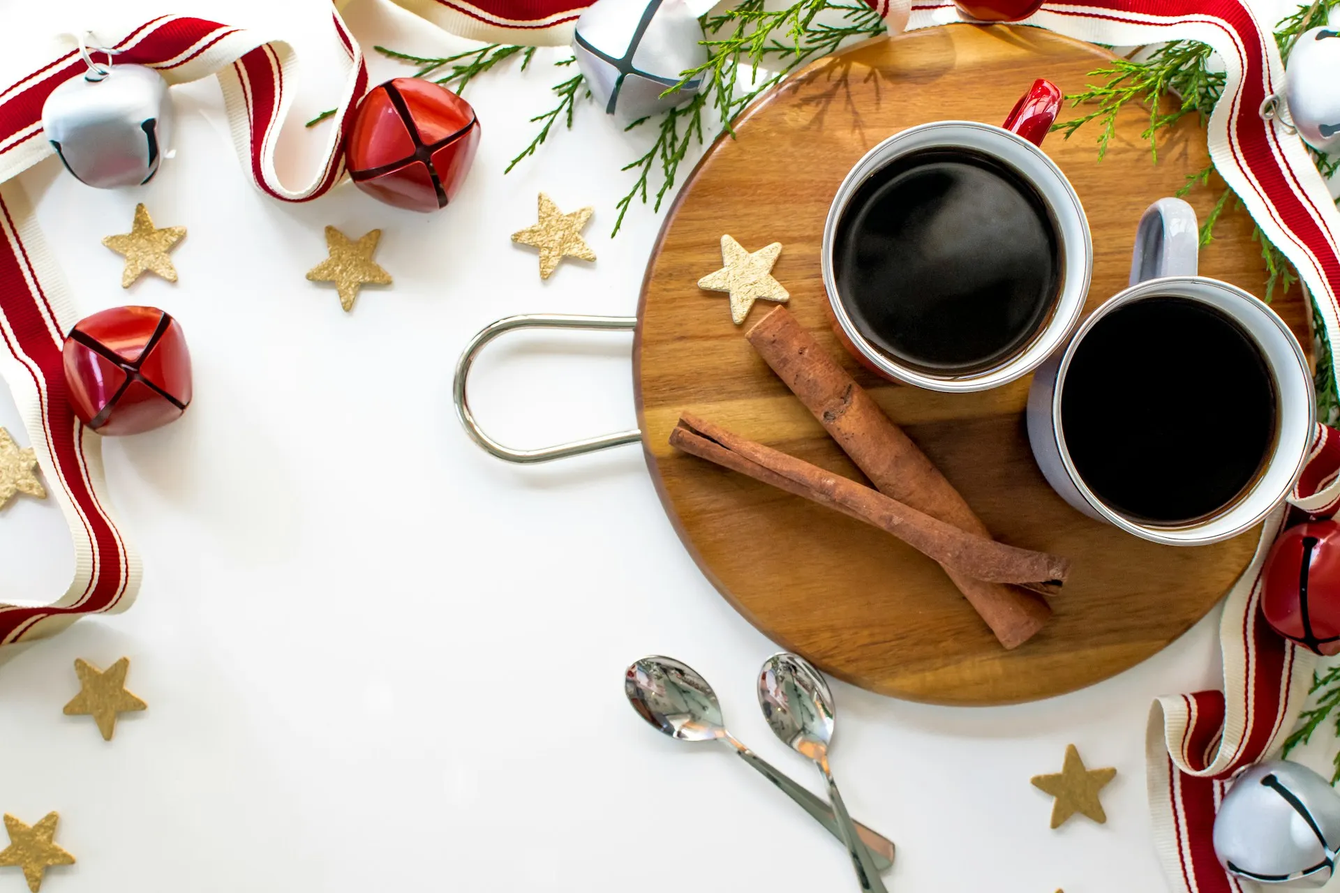 Zwei Tassen schwarzer Kaffee mit Zimtstangen auf einem Holzbrett zwischen Weihnachtsdeko