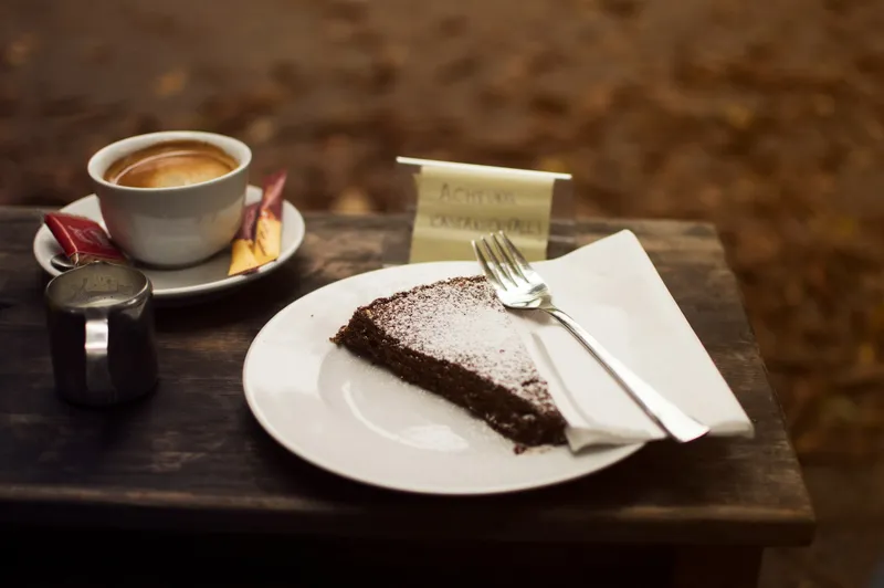 Ein Stück Schokoladenkuchen mit Puderzucker neben einer Tasse Kaffee