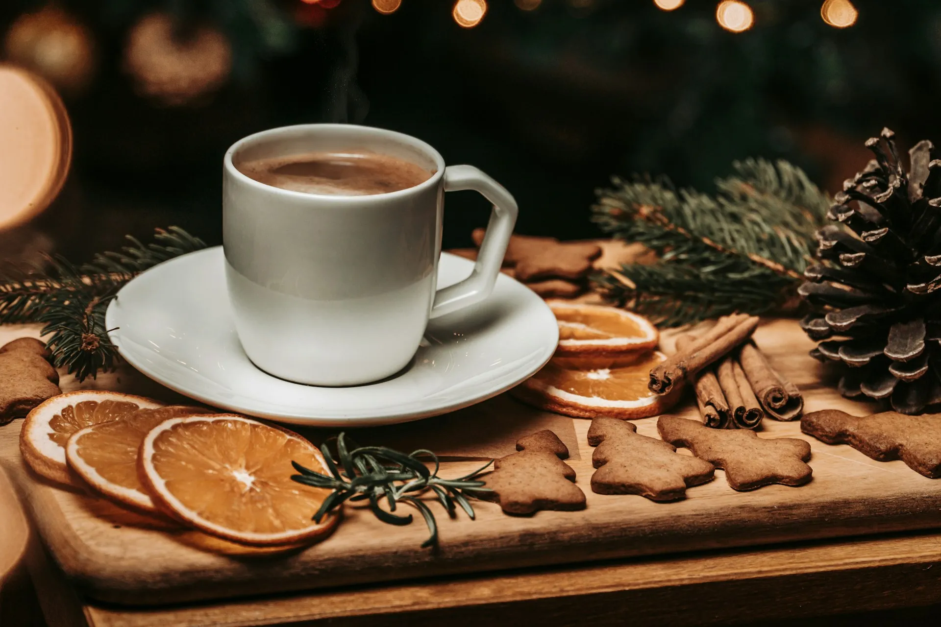 Eine Tasse Kaffee auf einem Holzbrett mit getrockneten Orangenscheiben, Zimtstangen und Lebkuchen