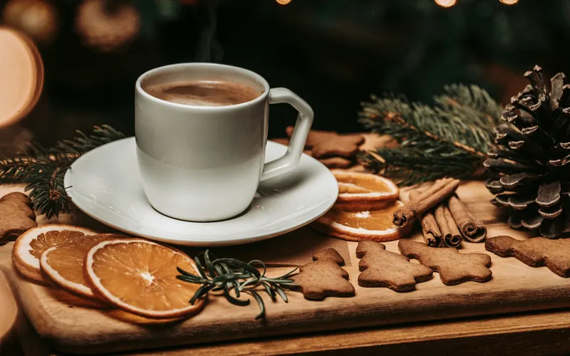 Eine Tasse Kaffee auf einem Holzbrett mit getrockneten Orangenscheiben, Zimtstangen und Lebkuchen